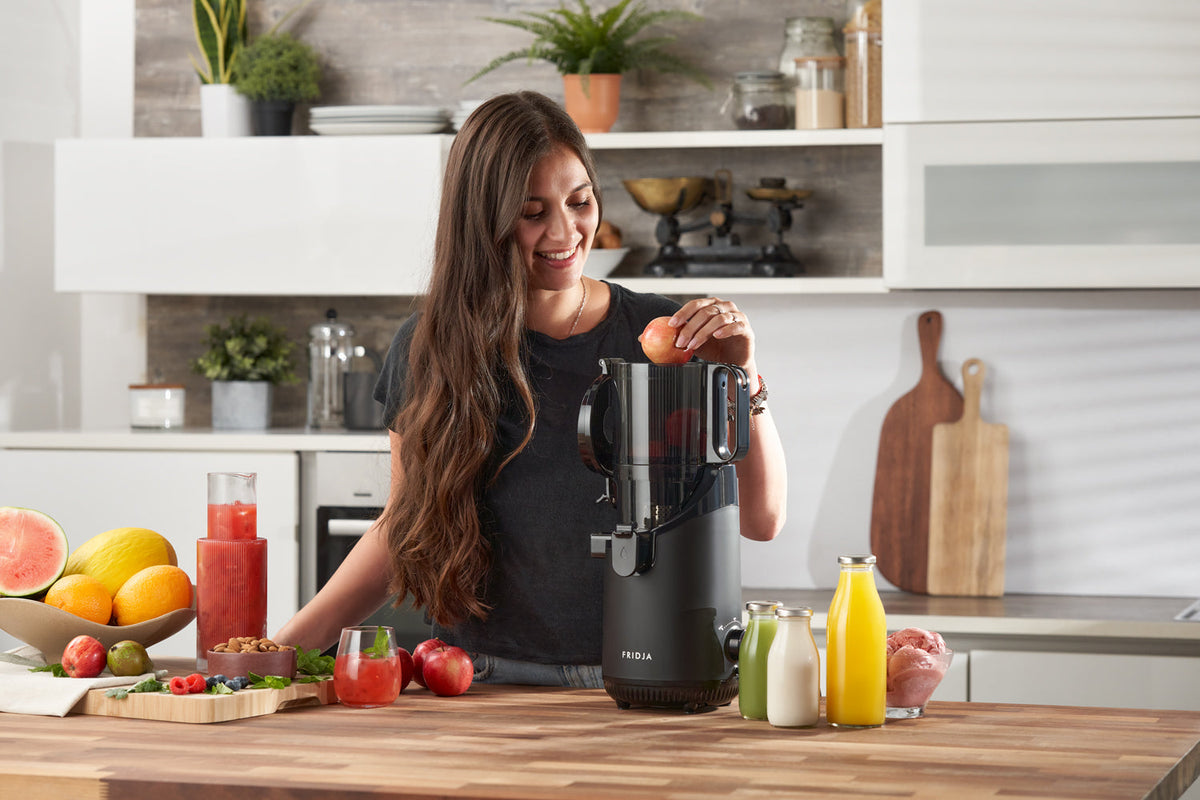 Woman feeding a whole apple into the Fridja f2500 self-feeding juicer in a kitchen