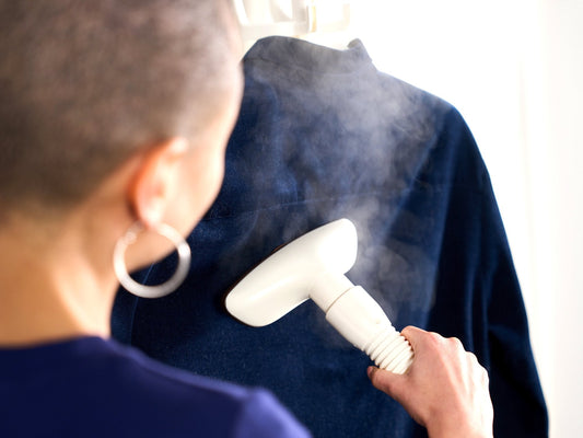 Steaming the back of a navy shirt with a white Fridja handheld steamer head