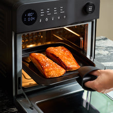 A person places a tray with two sesame-topped glazed salmon fillets into the Fridja f66 Super Oven - 15L Digital Air Fryer Oven, sets the convection mode to 180°C, and starts cooking.