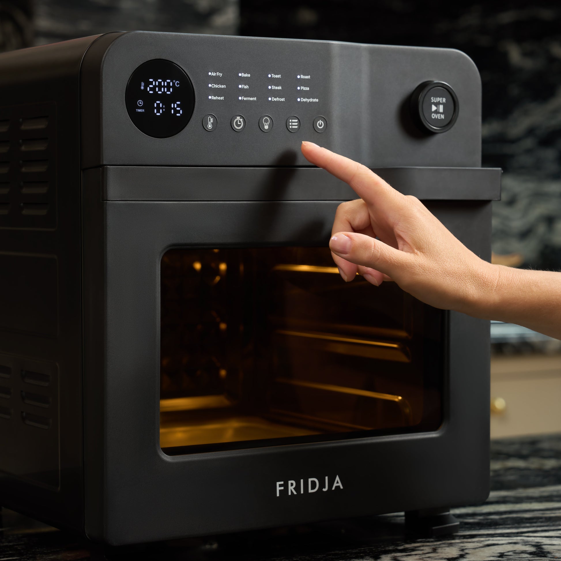 A hand presses a button on the control panel of the black Fridja f66 Super Oven 15L Digital Air Fryer Oven with digital display, PFAS free and ideal for convection cooking, in a modern kitchen.
