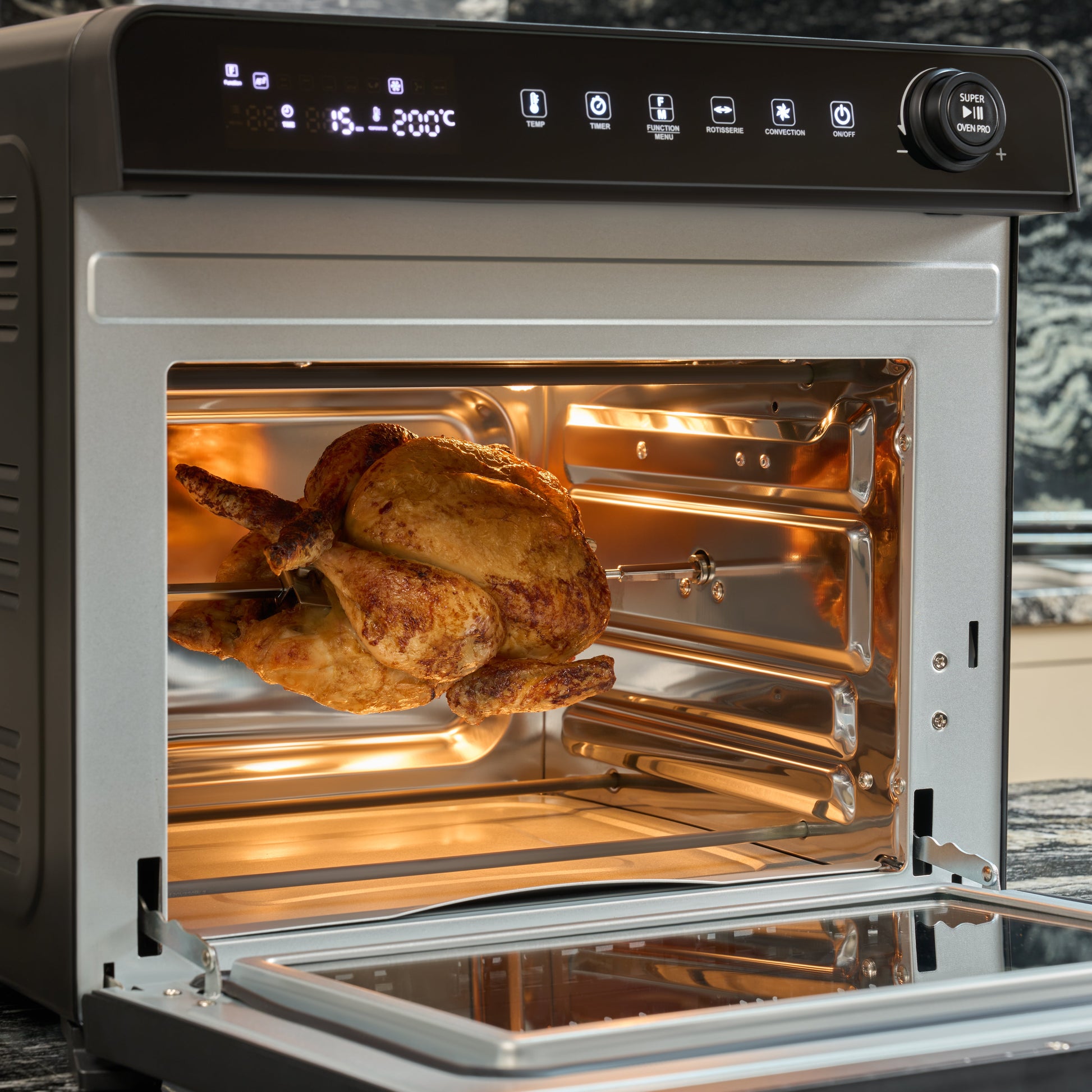 A whole roasted chicken rotates on a spit inside the Fridja f77 Super Oven Pro - 30L Digital Air Fryer Oven, its door open to reveal an illuminated interior and user-friendly digital controls.