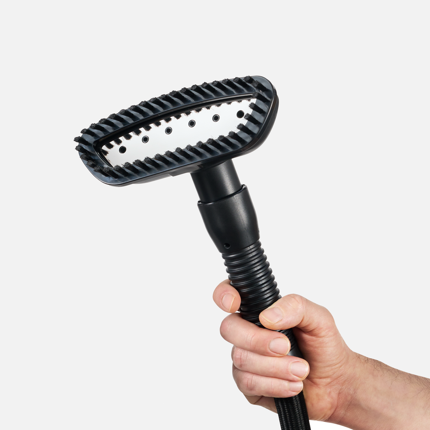 A hand holds a black Fridja f1200/f1600 Fabric Brush Attachment handheld garment steamer with a ribbed brush and visible steam holes, set against a plain white background.