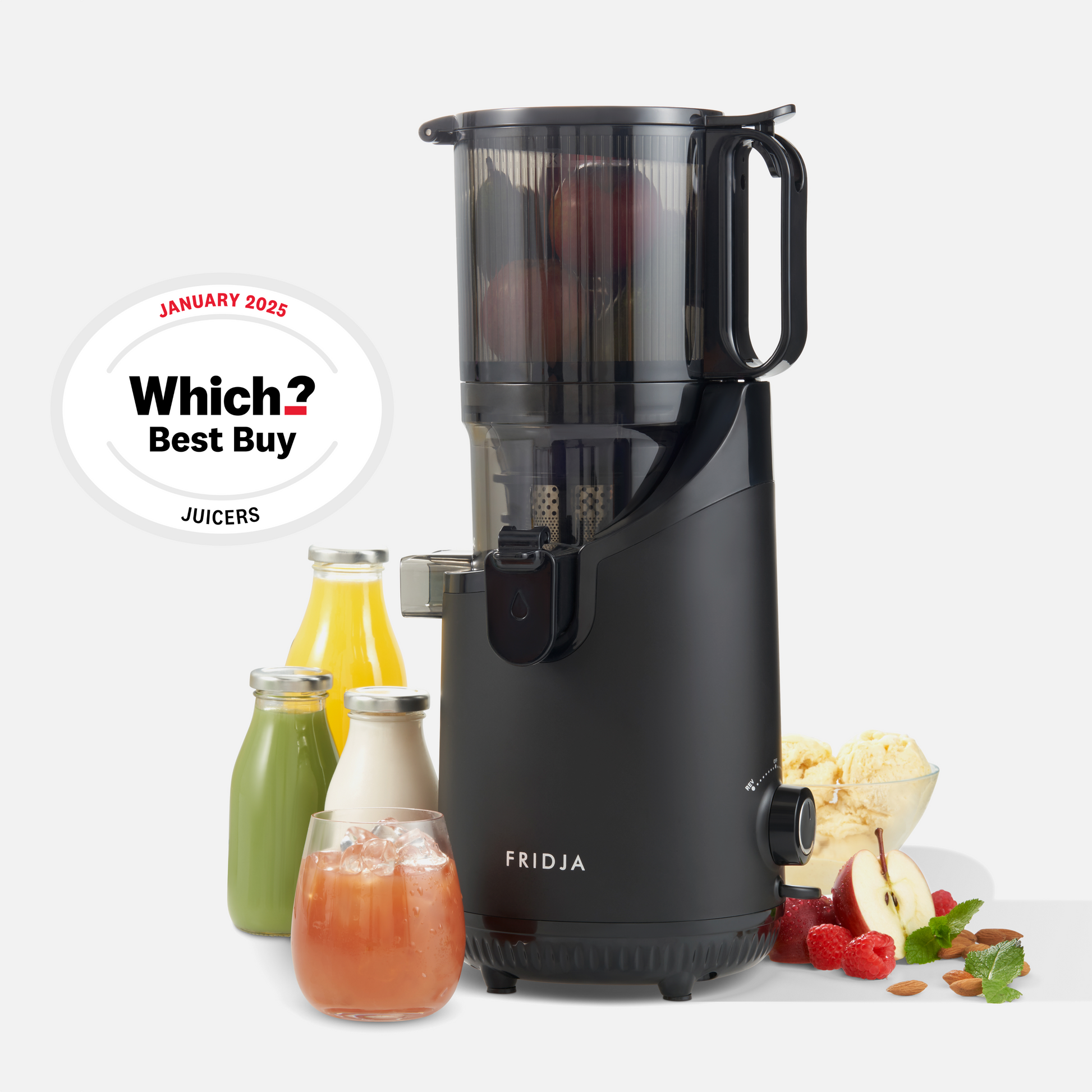 A Fridja f2500 Self Feeding Whole Fruit Juicer in black, filled with fruit, stands beside bottles and a glass of juice, surrounded by fruits and ice cream. A badge displays: Which? Best Buy Juicers January 2023.